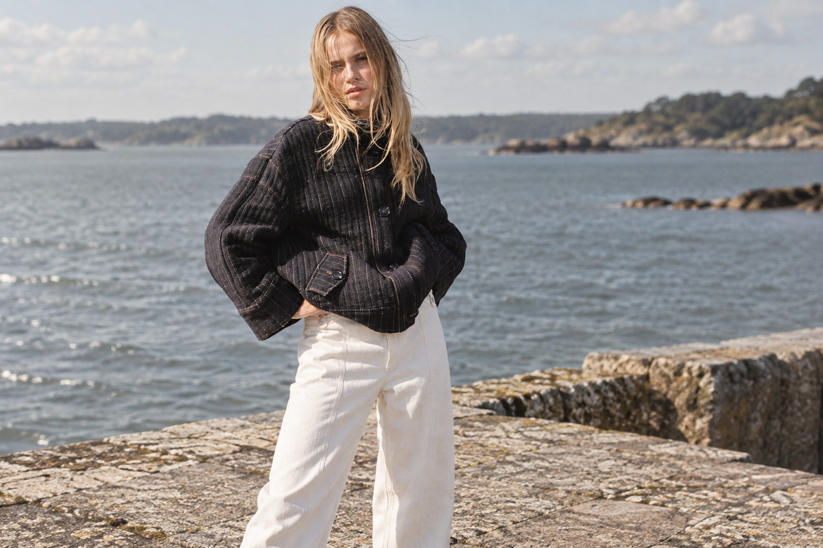 Veste Surfer Denim sombre à fines rayures portée avec un pantalon écru près d’un quai en granit.